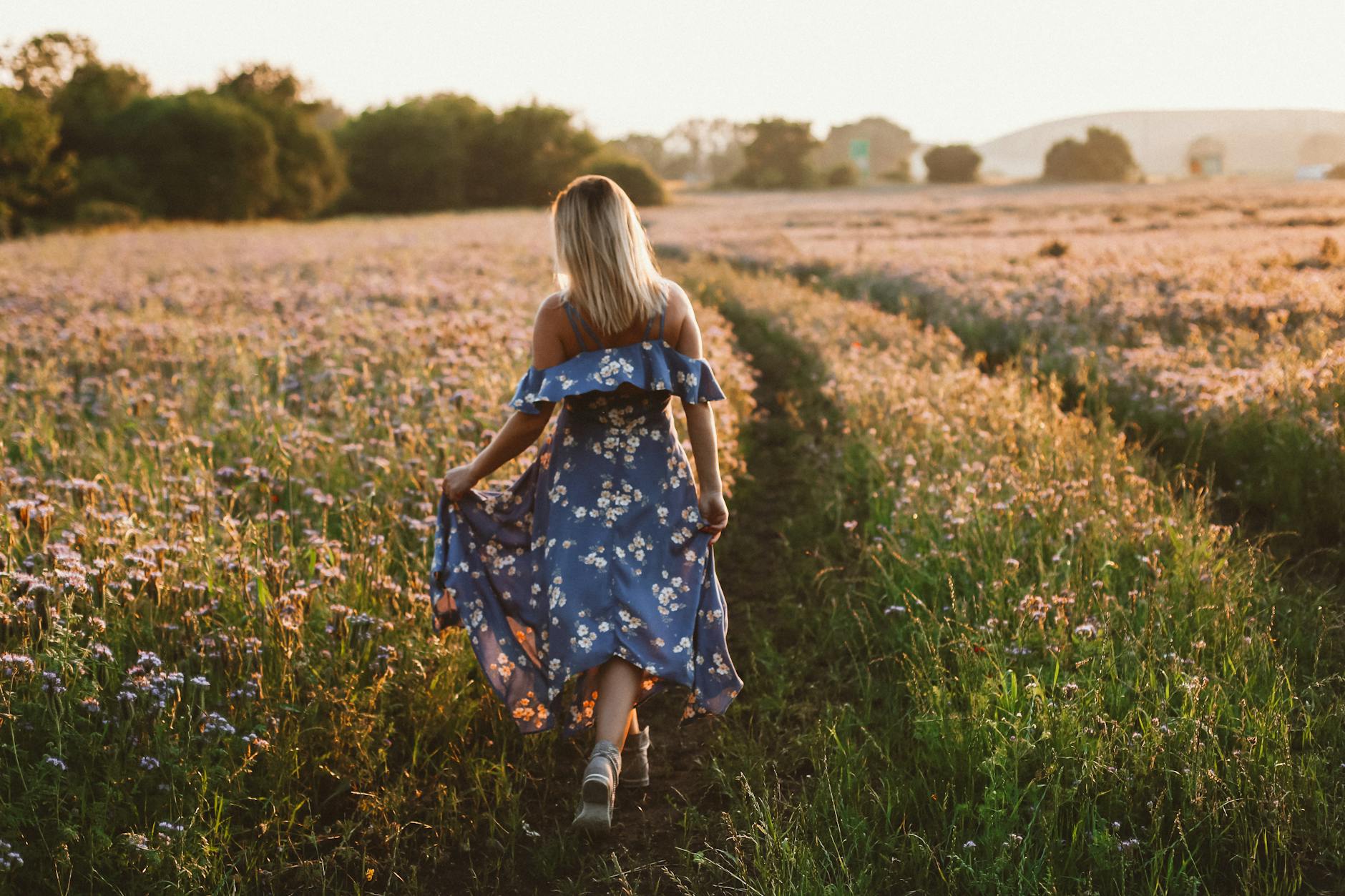 back view of a woman in a blue floral dress walking on a field with flowers