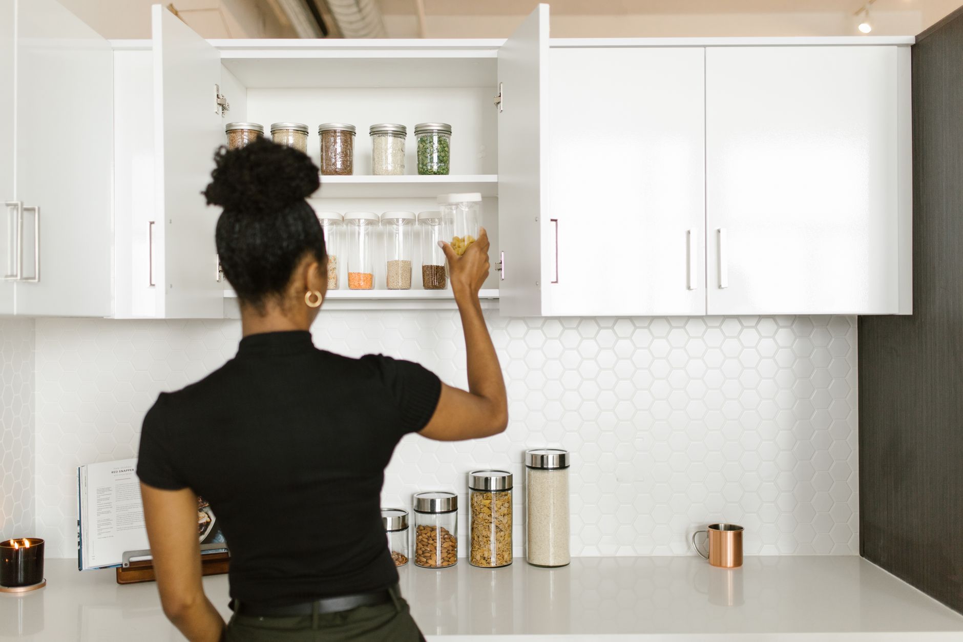 woman putting glass containers on a kitchen cabinet
