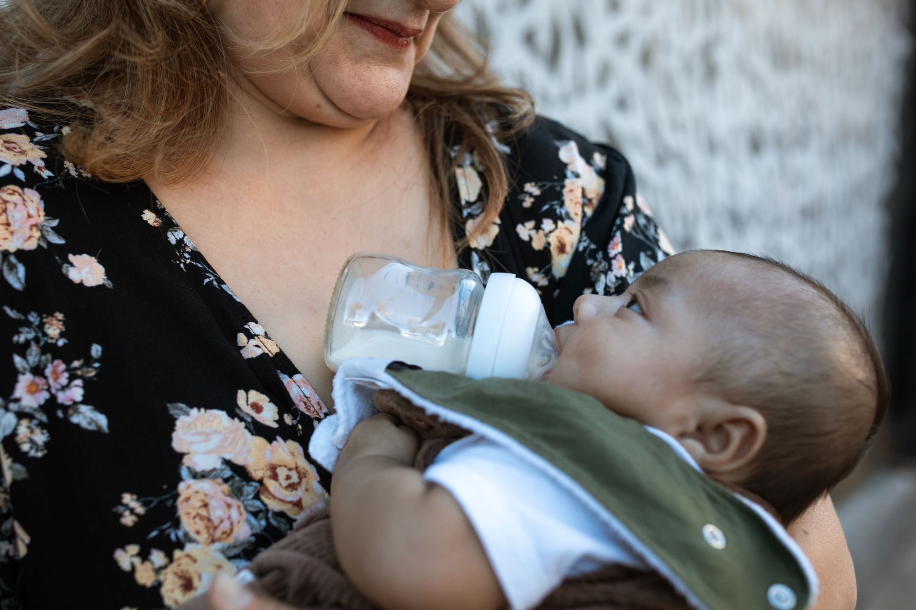 a woman in floral shirt carrying a baby while drinking milk